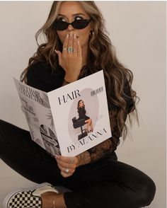 a woman sitting on the floor reading a book with her hands to her face and wearing sunglasses