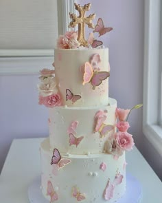 a three tiered cake with pink flowers and butterflies on the top, next to a window