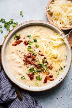 a bowl of soup with cheese and bacon in it next to two spoons on the side