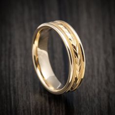 a gold wedding ring on a wooden table with black wood in the background and an engraved design