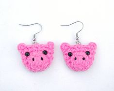 a pair of pink crocheted pig earrings with black eyes and ears on white background