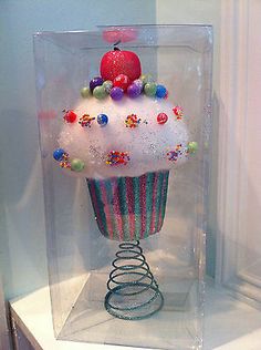 a cupcake in a glass case with colorful decorations on the top and bottom half