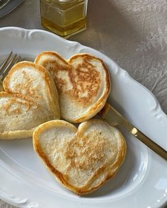 three heart shaped toasted breads on a white plate with a fork and honey jar