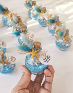 a hand holding a bottle filled with blue and gold glittered decorations on top of a table