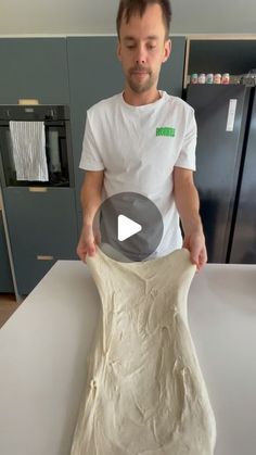 a man standing in front of a white counter top holding a piece of food that is shaped like a vase