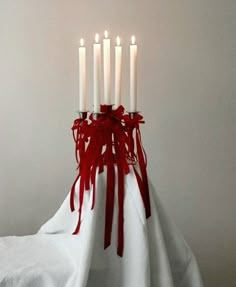 a bunch of candles that are on top of a white cloth with red ribbon around them