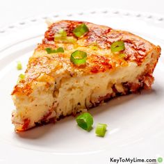 a slice of pizza on a white plate with green onions and cheese sprinkled on top