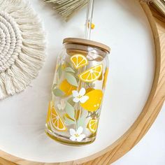 a glass jar with lemons and flowers on it next to a straw sun catcher