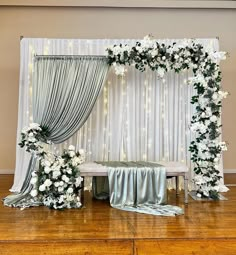 a decorated stage with white flowers and greenery on the side, along with silver drapes