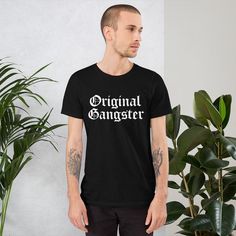 "Original Gangster shirt. Cholo style with old english text design.  Perfect gift shirt for OG street dudes of Latino heritage.  * 100% combed and ring-spun cotton  * Shoulder-to-shoulder taping * Side-seamed The Male model is wearing a size M. He's 6.2 feet (190 cm) tall, chest circumference 37.7\" (96 cm), waist circumference 33.4\" (85 cm). This shirt has been designed digitally by myself and is printed and shipped by Printful." Classic Cotton Shirt Pre-shrunk, Classic Logo Print Shirt For Streetwear, Classic Logo Print Streetwear Shirt, Classic Cotton Shirt With Letter Print, Classic Streetwear T-shirt With Screen Print, Classic Shirt With Graphic Print For Streetwear, Classic Graphic Print Shirt For Streetwear, Classic Short Sleeve Pre-shrunk Shirt, Classic Streetwear Tops With Text Print