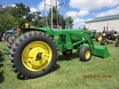 a large green tractor parked on top of a lush green field next to other farm equipment