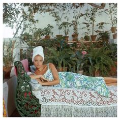 a woman laying on top of a bed next to potted plants