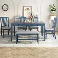 a blue table and chairs in a room with white walls, wood flooring and a clock on the wall