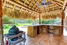 an outdoor kitchen with a grill and table under a thatch roof over looking the pool