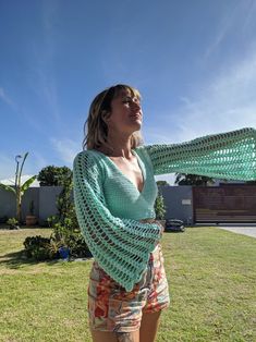 a woman standing on top of a lush green field holding a crocheted shawl