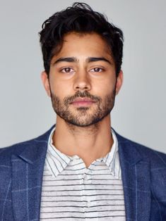 a man in a blue jacket and striped shirt looking at the camera with a serious look on his face