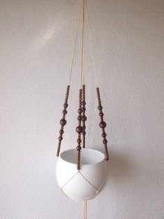 a white vase with beads hanging from it's sides on a wall next to a wooden bead necklace