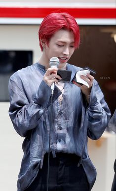 a man with red hair is holding a microphone and looking at his cell phone while standing in front of a building