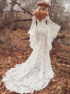 a woman in a white dress and hat is walking through the leaves with her back to the camera