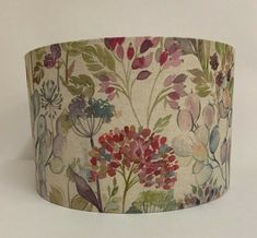 a lampshade with flowers and leaves on the fabric, hanging from a wall