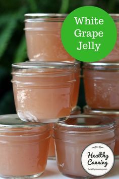 four jars filled with white grape jelly sitting on top of a table next to green plants