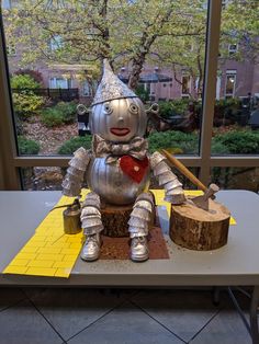 a metal robot sitting on top of a table next to a tree stump with a hammer