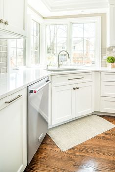 a clean kitchen with white cabinets and wood flooring is pictured in this image, the dishwasher has been left open