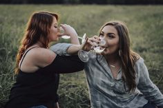 two women sitting in a field drinking wine from wine glasses with their mouths wide open