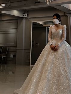 a woman in a wedding dress wearing a face mask standing next to a chandelier