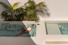 a woman laying on top of a green and white striped couch next to a swimming pool