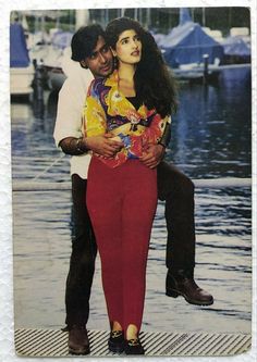 a man is holding a woman on his back in front of the water and boats