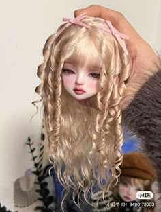 a doll with long blonde hair is being held by someone