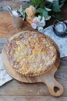 a pie sitting on top of a wooden cutting board next to a vase with flowers