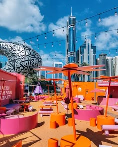 an outdoor seating area with bright pink and orange chairs, umbrellas and lights strung from the ceiling