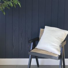 a white pillow sitting on top of a wooden chair next to a green plant in front of a blue wall