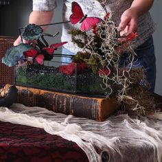 a woman is arranging flowers in a vase on top of an old book with moss