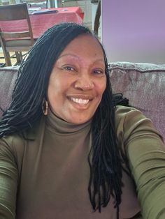 a woman with dreadlocks sitting on a couch smiling at the camera and looking into the camera