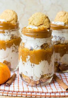 three jars filled with desserts sitting on top of a table next to an orange pumpkin