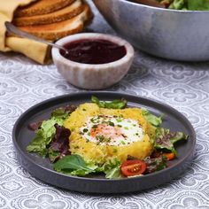 a black plate topped with food next to a bowl filled with fruit and veggies