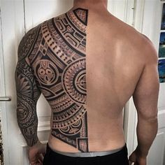 a man with a tattoo on his back is standing in front of a door and looking at the wall