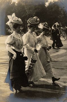 an old black and white photo of women walking down the street with hats on their heads