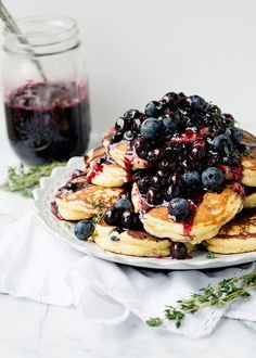 pancakes with blueberries and syrup are on a plate next to a jar of jam