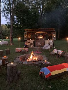 an outdoor fire pit with candles lit up in the night time, surrounded by chairs and blankets