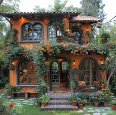 an orange house with lots of flowers on the front and side windows, surrounded by greenery