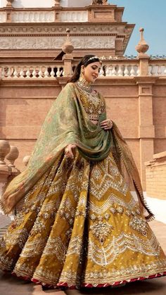 a woman in a yellow and green lehenga is standing on the ground with her hands behind her back