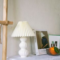 a white lamp sitting on top of a table next to a book and an orange