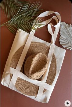 a straw hat sits on top of a white tote bag next to a palm leaf