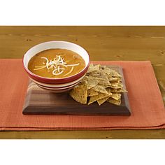 a bowl of soup and some crackers on a wooden tray with an orange place mat