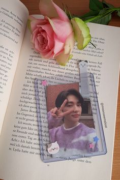 a pink rose sitting on top of an open book next to a photo and pen