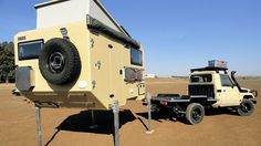 an off - road vehicle is parked next to a camper trailer in the desert